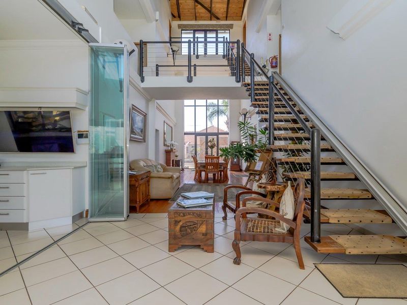 Spacious open-plan living area featuring a double-volume ceiling with exposed timber beams, a central staircase with a stairlift, and mezzanine level access.