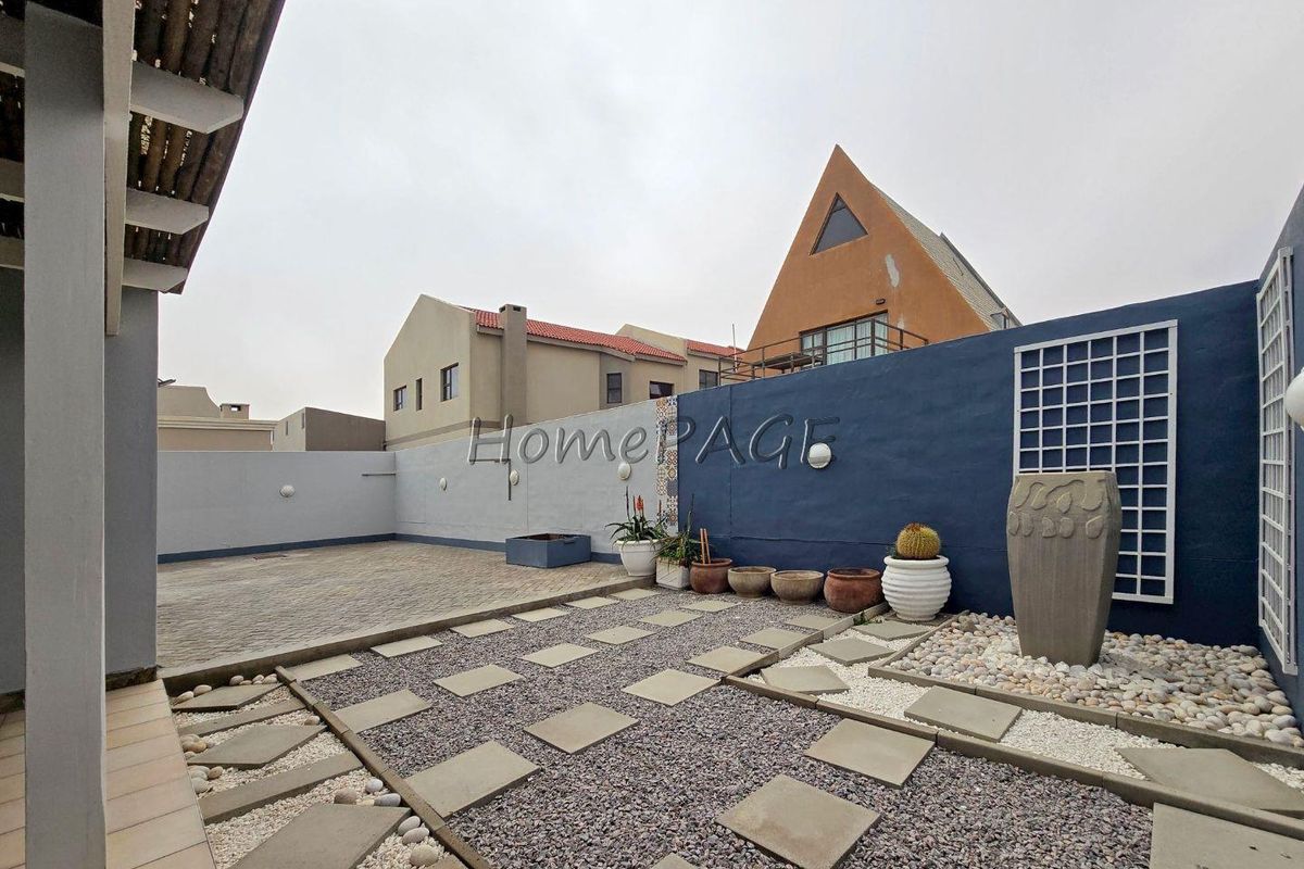 A low-maintenance rear courtyard featuring paved areas, gravel landscaping with stone pavers, and a decorative boundary wall.