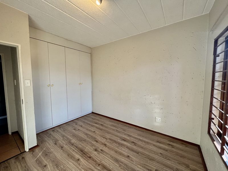An empty bedroom featuring laminate flooring, built-in cupboards, and security burglar bars on the window.