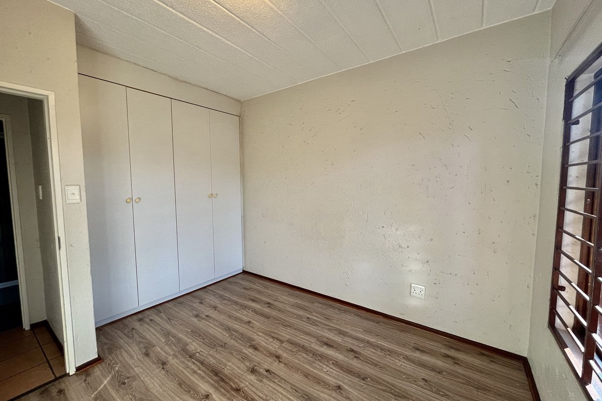 An empty bedroom featuring laminate flooring, built-in cupboards, and security burglar bars on the window.