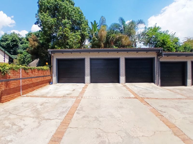 A triple garage unit featuring dark sectional doors, set against a paved driveway with brick detailing and perimeter security fencing.