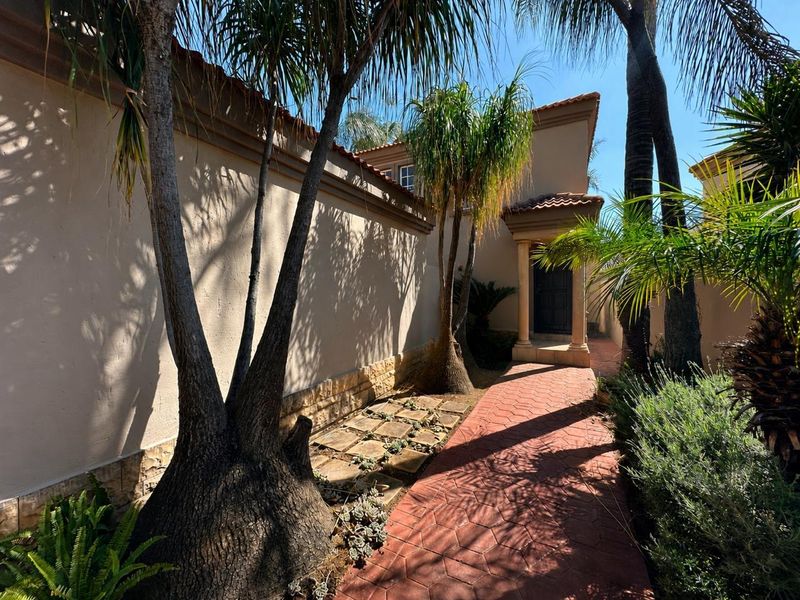 A well-maintained front entrance pathway featuring decorative stone cladding, stucco walls, and a covered portico surrounded by established landscaping.