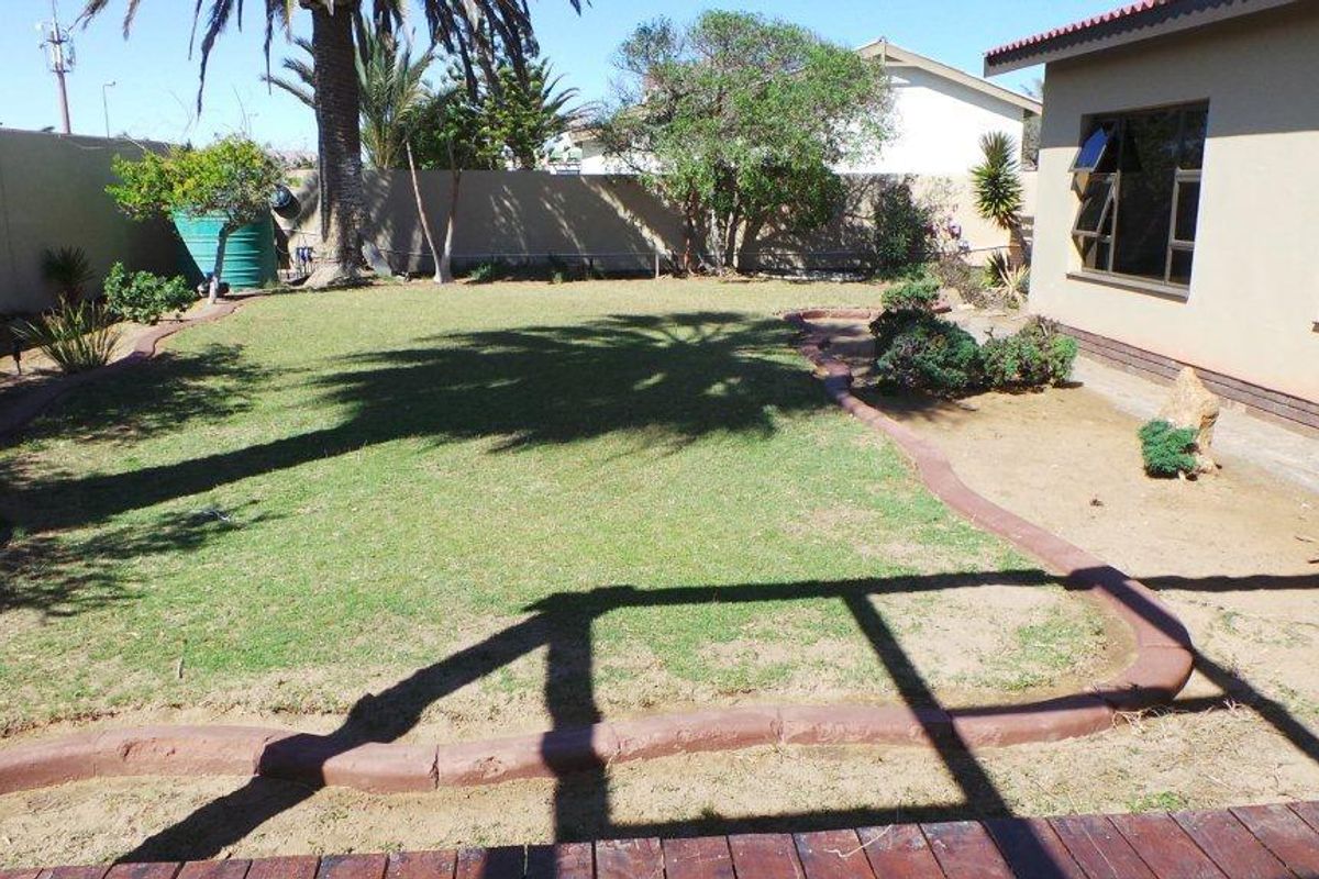 A spacious rear garden featuring a manicured lawn, established trees, and a perimeter wall, providing a private outdoor space for relaxation.