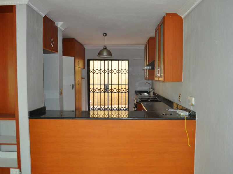 A functional galley-style kitchen featuring wood-finish cabinetry, granite countertops, and a security gate leading to the exterior.