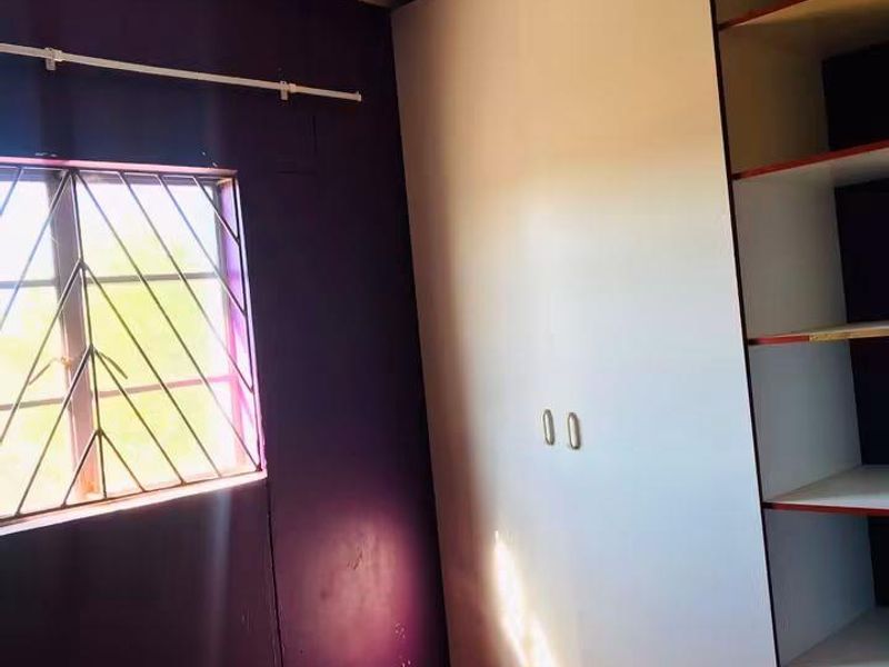 A bedroom featuring tiled flooring, a built-in wardrobe with open shelving, and a window fitted with security bars.
