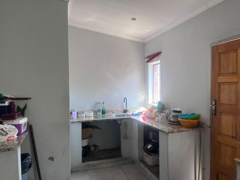 A functional kitchen area featuring granite countertops, a stainless steel sink, and tiled flooring, currently requiring cosmetic updates and cabinet installation.