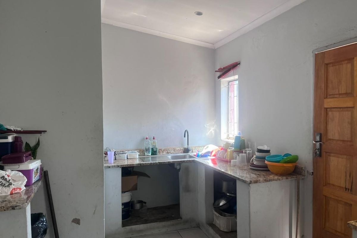 A functional kitchen area featuring granite countertops, a stainless steel sink, and tiled flooring, currently requiring cosmetic updates and cabinet installation.