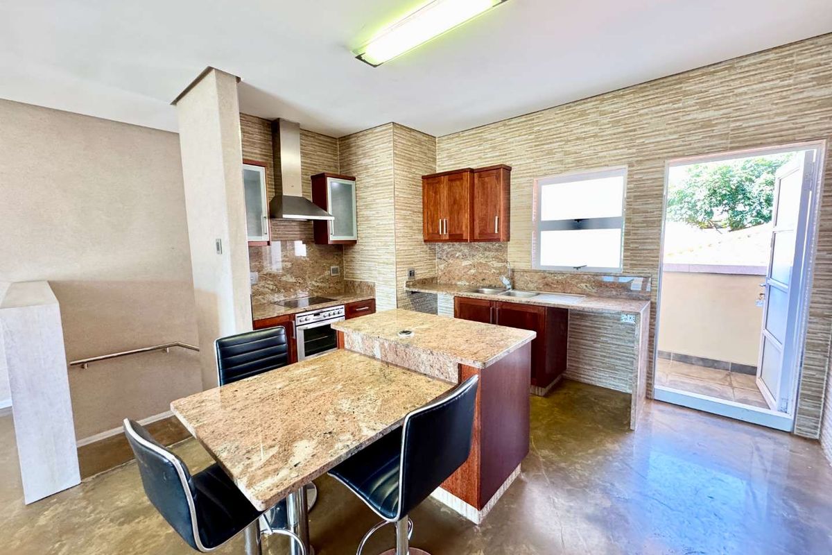 Kitchen featuring granite countertops, wooden cabinetry, stainless steel extractor fan, and an integrated breakfast bar, with direct access to an outdoor balcony area.