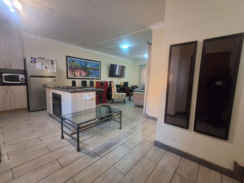 Open-plan living area featuring a kitchen with island, built-in oven, and hob, seamlessly flowing into the lounge space with tiled flooring throughout.