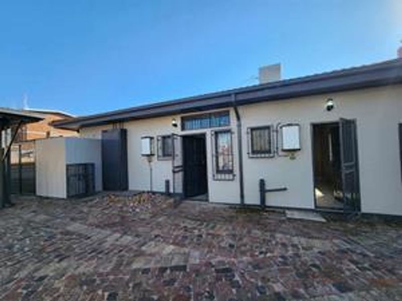 Rear exterior view of the apartment featuring a paved courtyard, security gates, and external wall lighting.