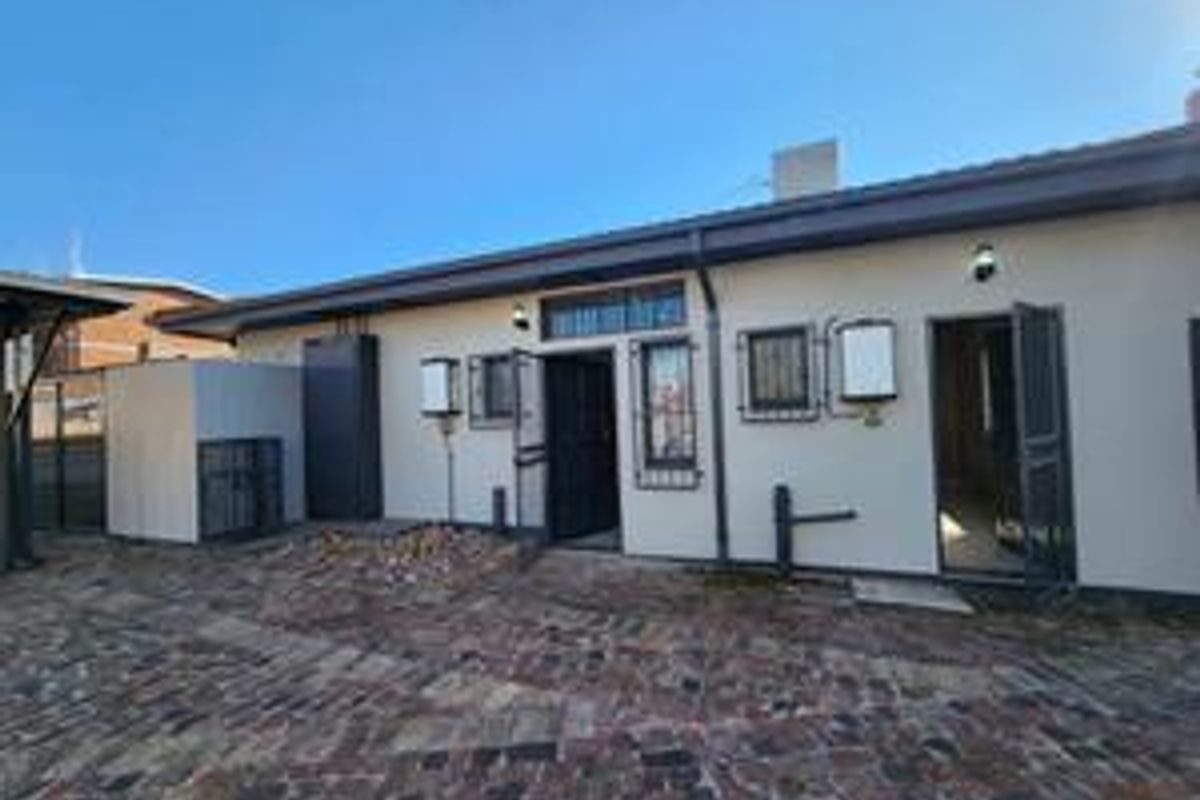 Rear exterior view of the apartment featuring a paved courtyard, security gates, and external wall lighting.