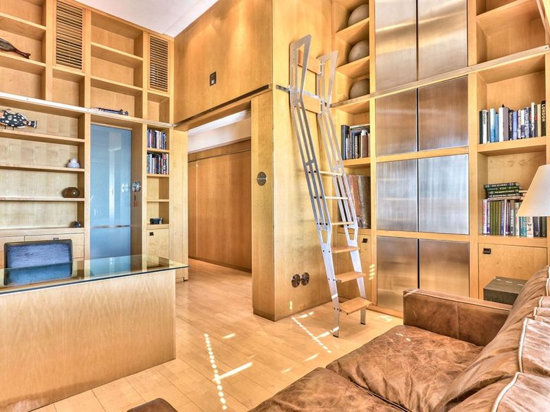 A sophisticated home office featuring extensive custom floor-to-ceiling wooden shelving, integrated metal storage cabinets, and a functional sliding library ladder.