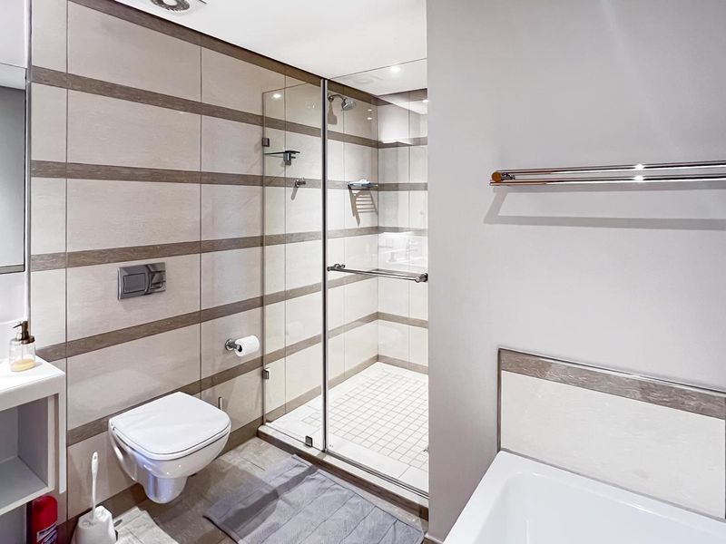 Modern bathroom featuring a wall-mounted toilet, glass-enclosed shower, and contemporary tiled finishes with integrated vanity and towel rail.