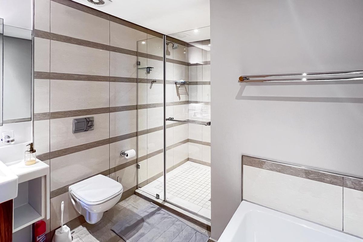 Modern bathroom featuring a wall-mounted toilet, glass-enclosed shower, and contemporary tiled finishes with integrated vanity and towel rail.