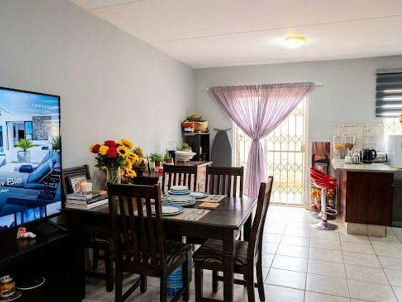 Open-plan living and dining area featuring tiled flooring, kitchen cabinetry with countertops, and a security gate leading to the exterior.
