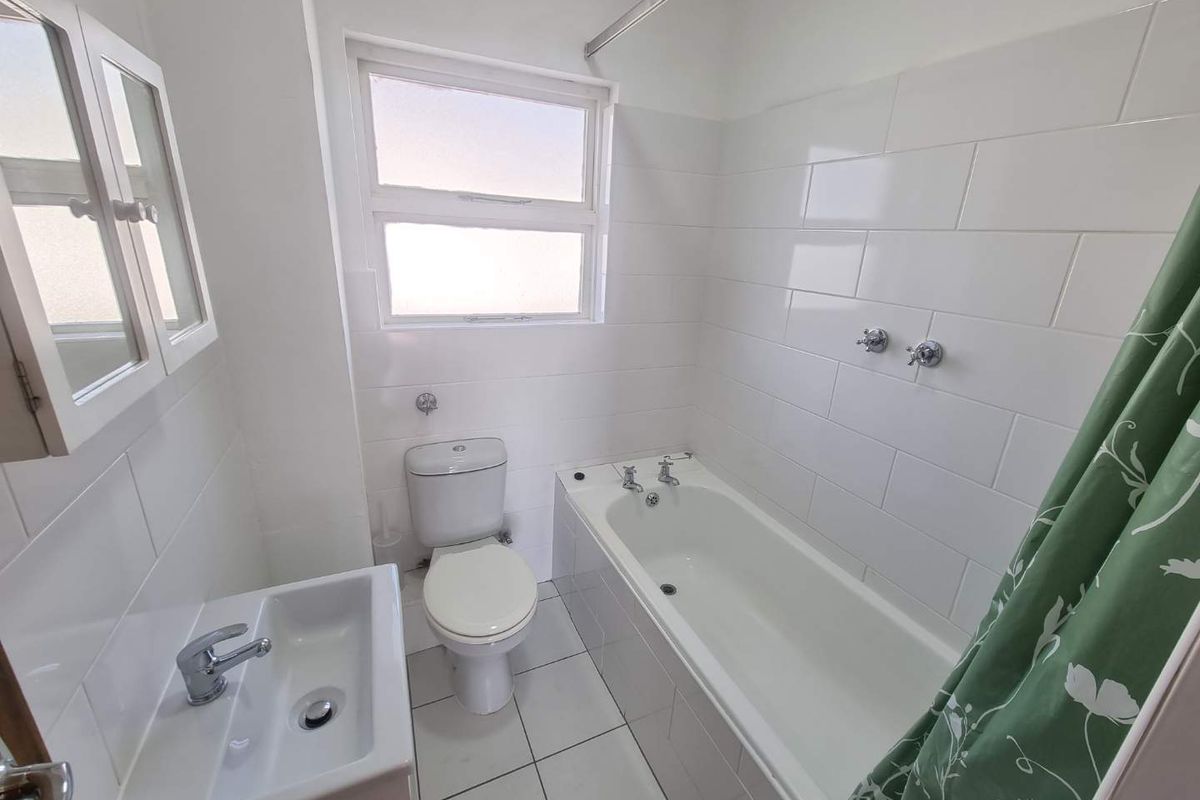 A clean, functional bathroom featuring white wall tiles, a standard bathtub with shower mixer, a toilet, and a wall-mounted washbasin with a medicine cabinet.