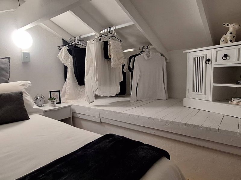 Cozy attic-style bedroom featuring sloped ceilings with exposed rafters, built-in shelving, and a dedicated hanging area for clothing.