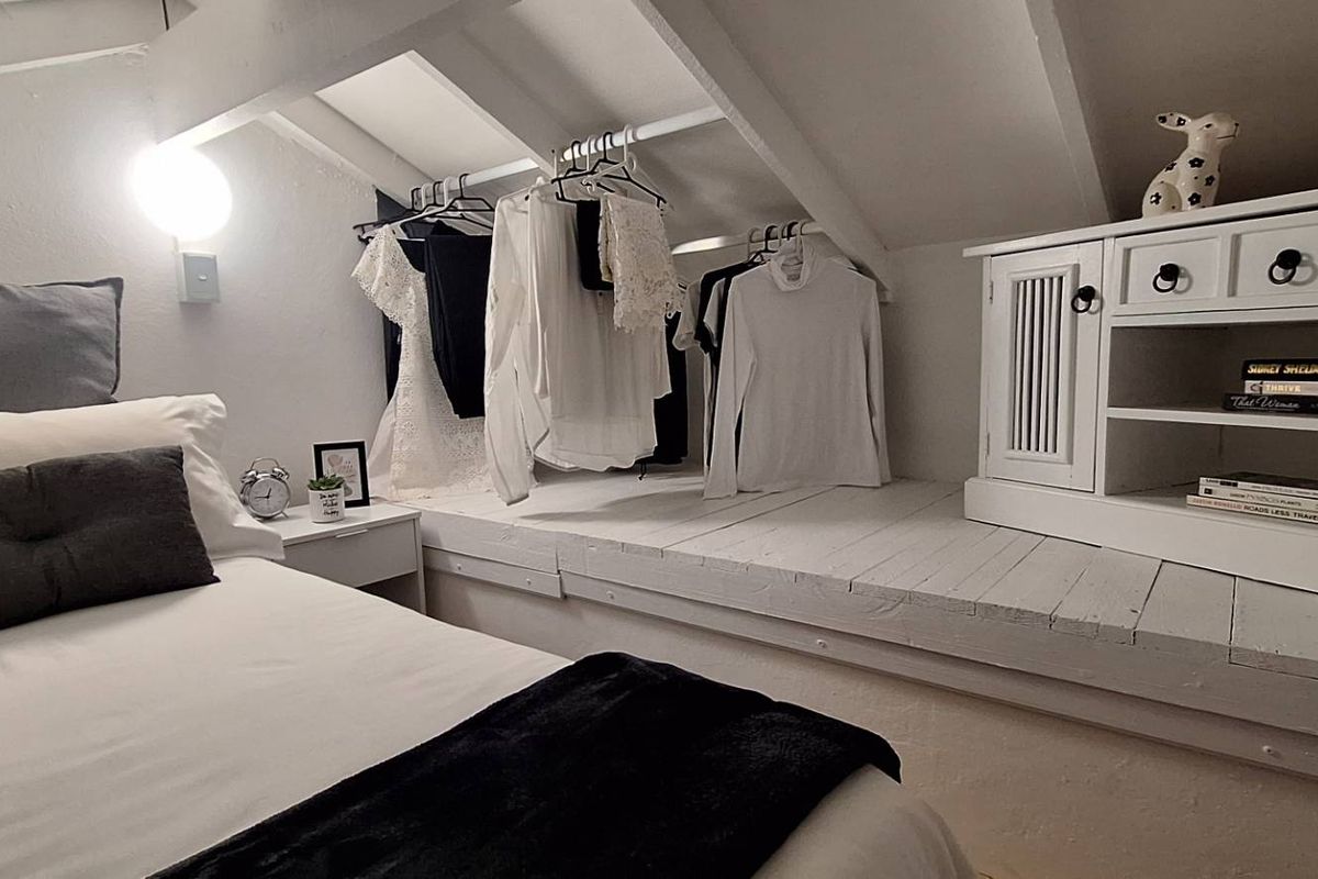 Cozy attic-style bedroom featuring sloped ceilings with exposed rafters, built-in shelving, and a dedicated hanging area for clothing.