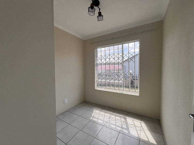 A bright, empty bedroom featuring neutral wall paint, tiled flooring, and a window fitted with a security gate.