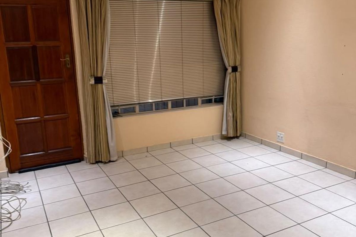 An empty living room featuring neutral tiled flooring, a ceiling fan, and a timber panel door with natural light provided by a window with blinds.