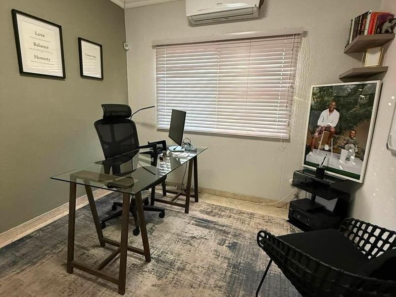 A functional home office space featuring tiled flooring, a wall-mounted air conditioning unit, and venetian blinds for light control.