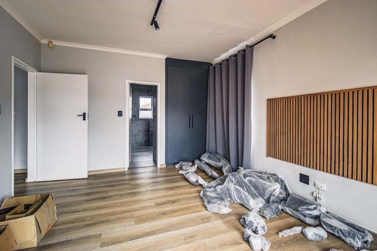 A modern bedroom featuring wood-look flooring, built-in cabinetry, a decorative timber wall panel, and an en-suite bathroom entrance.