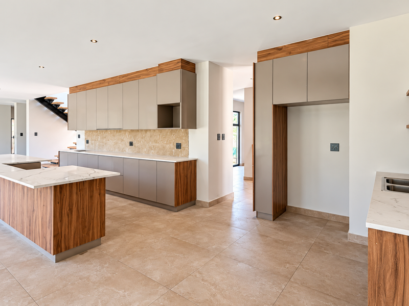 Modern, spacious kitchen featuring a large island with stone countertops, sleek cabinetry, floating shelves, and high-quality tiled flooring in an open-plan layout.