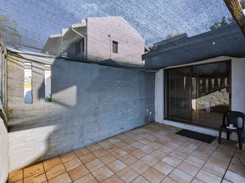 A private outdoor patio area featuring tiled flooring, a shade cloth canopy, and direct access to the interior via a sliding glass door.