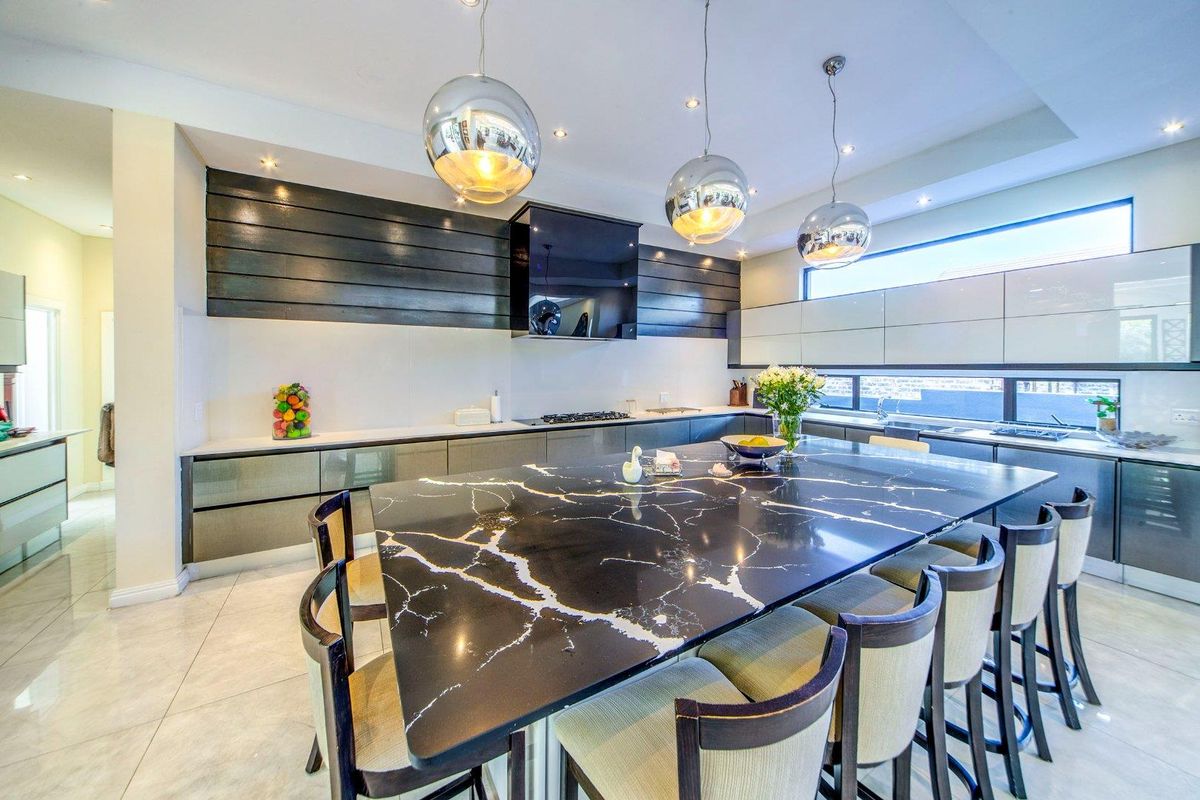 Modern kitchen featuring a large black marble-topped island, sleek cabinetry, integrated appliances, and contemporary pendant lighting.