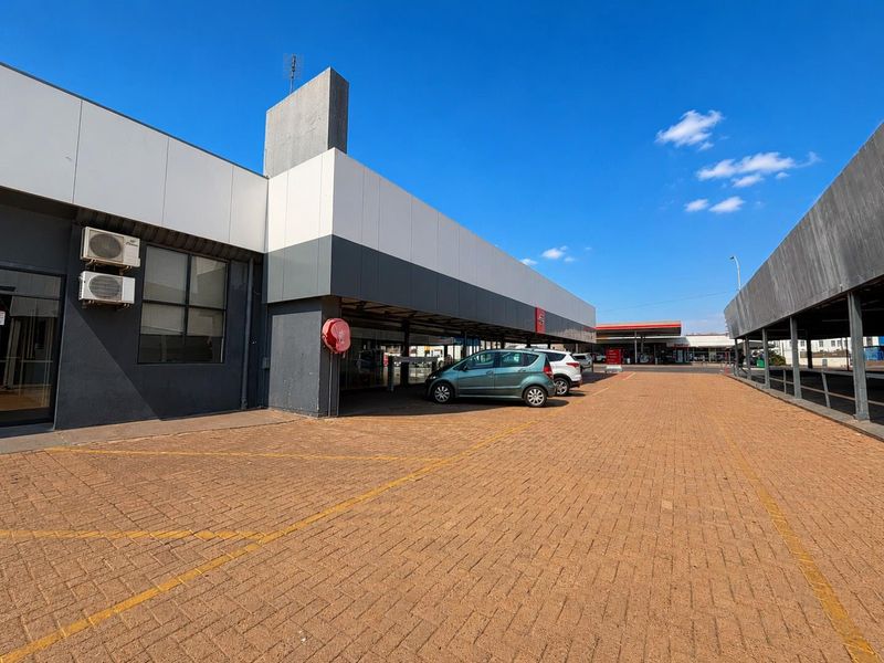 Exterior view of a commercial property featuring a paved parking area, covered bays, and wall-mounted air conditioning units.