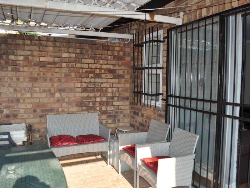 A covered outdoor patio area featuring exposed brick walls, paved flooring, and security fixtures, providing a functional space for outdoor relaxation.