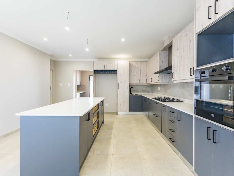 Modern kitchen featuring a large island, quartz countertops, built-in oven, gas hob, and contemporary two-tone cabinetry with ample storage space.