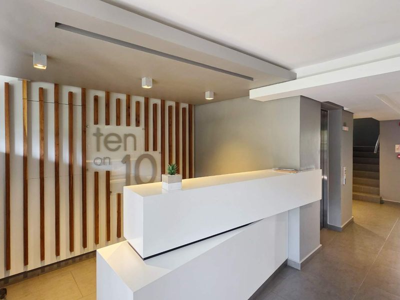 Modern apartment building entrance lobby featuring a sleek reception desk, decorative timber wall paneling, and elevator access.