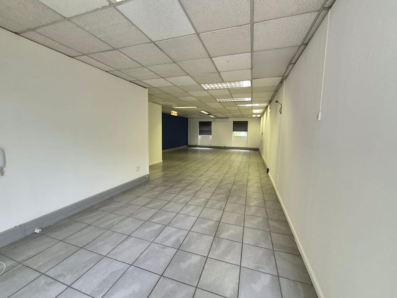 An open-plan office space featuring ceramic floor tiles, a suspended ceiling with recessed lighting, and an integrated air conditioning unit.