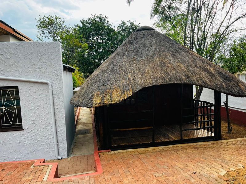 A rear garden area featuring a traditional thatched-roof structure with a timber deck, adjacent to a paved walkway and main building exterior.