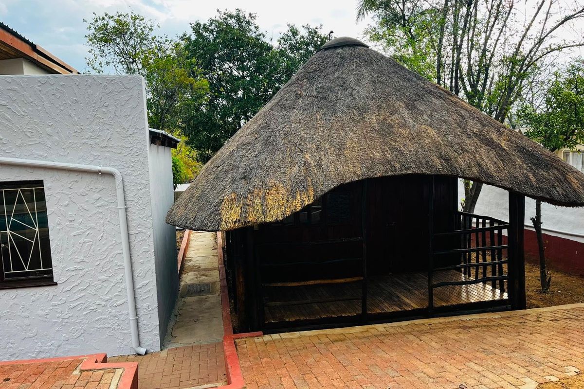 A rear garden area featuring a traditional thatched-roof structure with a timber deck, adjacent to a paved walkway and main building exterior.