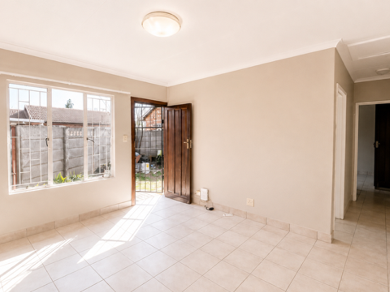 A bright, empty living area featuring tiled flooring, a security gate, and direct access to the exterior.