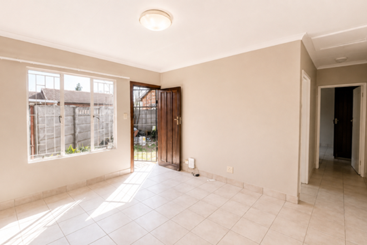 A bright, empty living area featuring tiled flooring, a security gate, and direct access to the exterior.