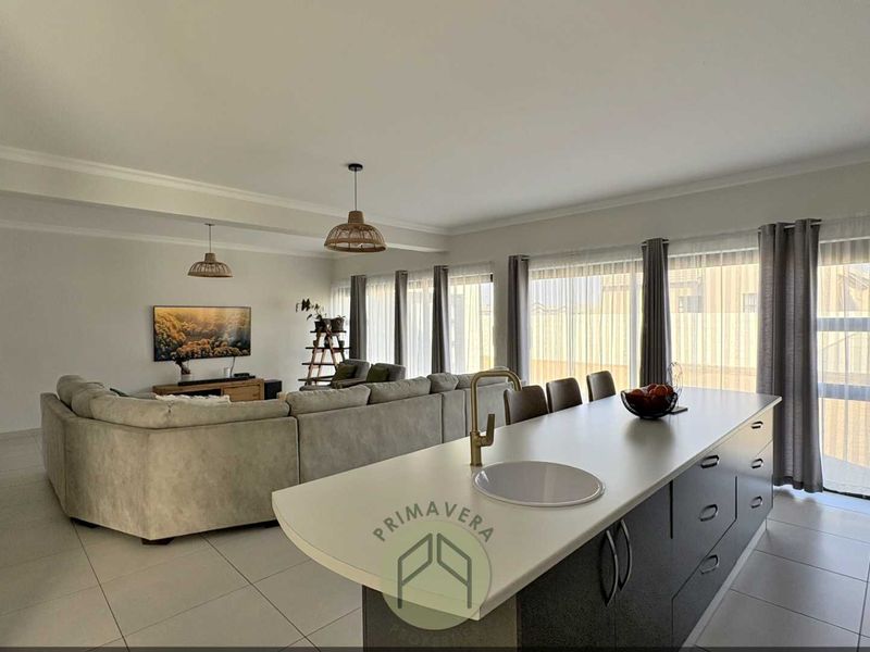 Spacious open-plan living area featuring a modern kitchen island with a brass faucet, tiled flooring, and large sliding doors providing ample natural light.