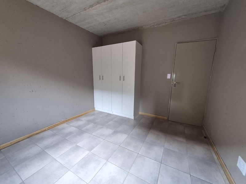 A minimalist bedroom featuring tiled flooring, an exposed concrete ceiling, and a built-in white wardrobe.