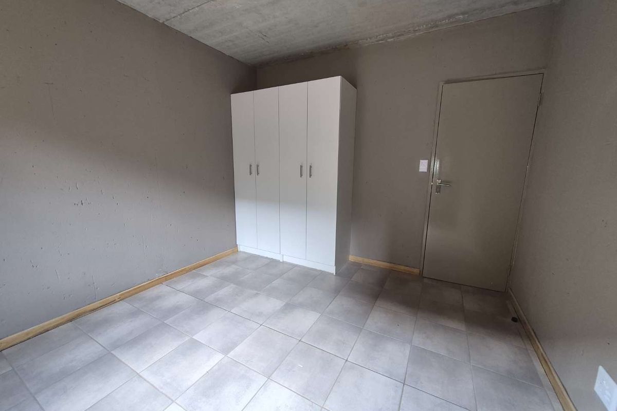 A minimalist bedroom featuring tiled flooring, an exposed concrete ceiling, and a built-in white wardrobe.