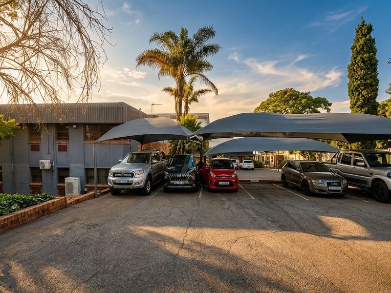Exterior view of a business property featuring a paved parking area with multiple shade cloth carports and a brick retaining wall.