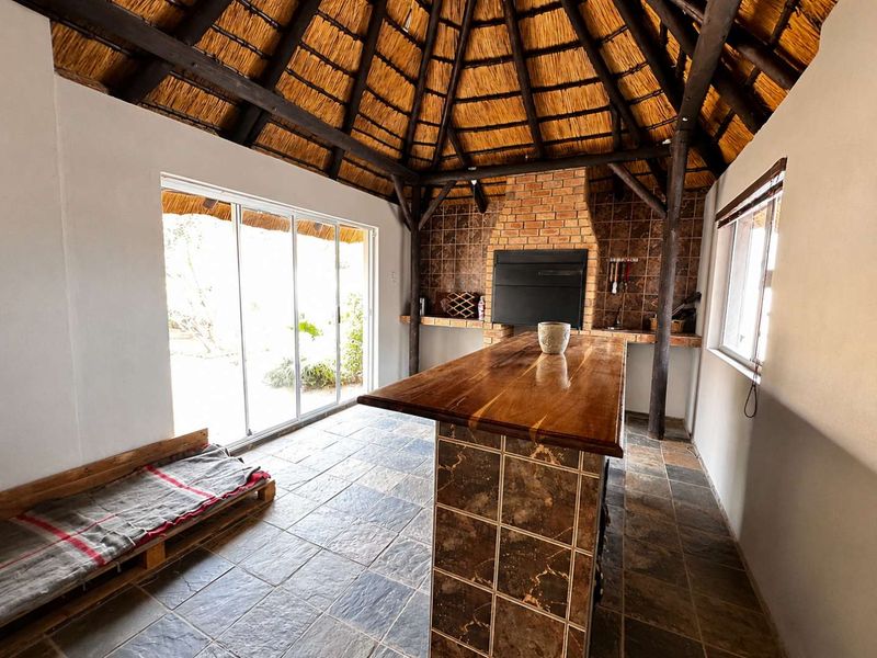 Covered outdoor entertainment area featuring a traditional thatched roof, built-in brick braai, and a central tiled island with slate flooring.