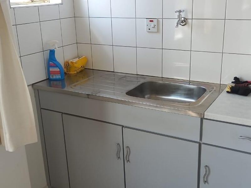 A functional laundry area featuring a stainless steel sink, built-in cabinetry, and tiled splashback.