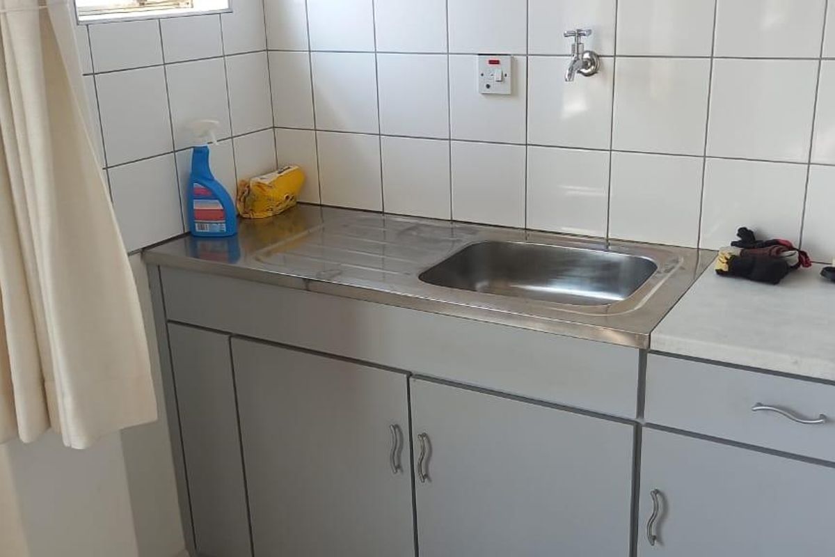 A functional laundry area featuring a stainless steel sink, built-in cabinetry, and tiled splashback.