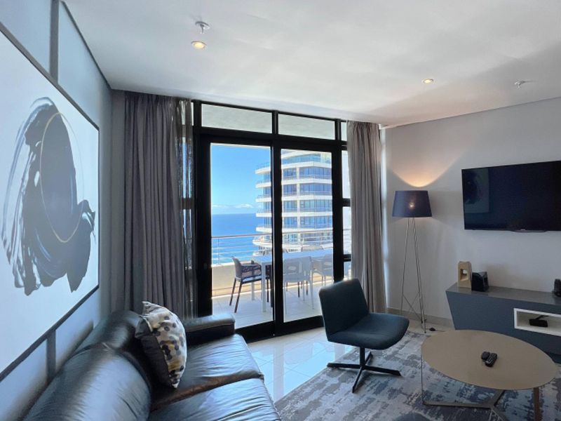 Modern living room featuring tiled floors, recessed lighting, and large sliding glass doors opening onto a balcony with ocean views.