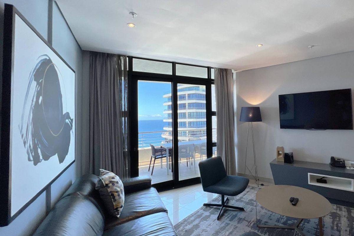 Modern living room featuring tiled floors, recessed lighting, and large sliding glass doors opening onto a balcony with ocean views.