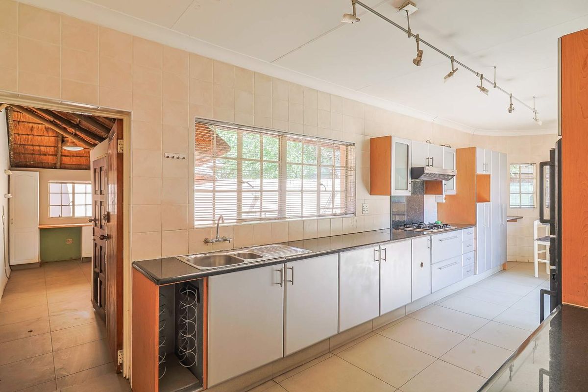 A functional kitchen featuring a long granite countertop, double stainless steel sink, built-in hob, extractor fan, and ample cabinetry, with an adjacent utility area.