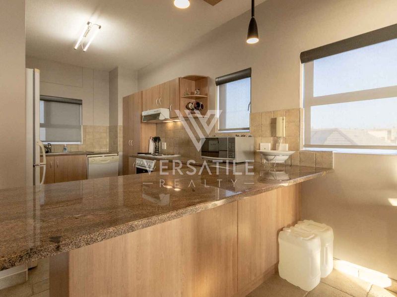 A functional kitchen featuring light wood cabinetry, granite countertops, a breakfast bar, and a tiled backsplash with ample natural light.