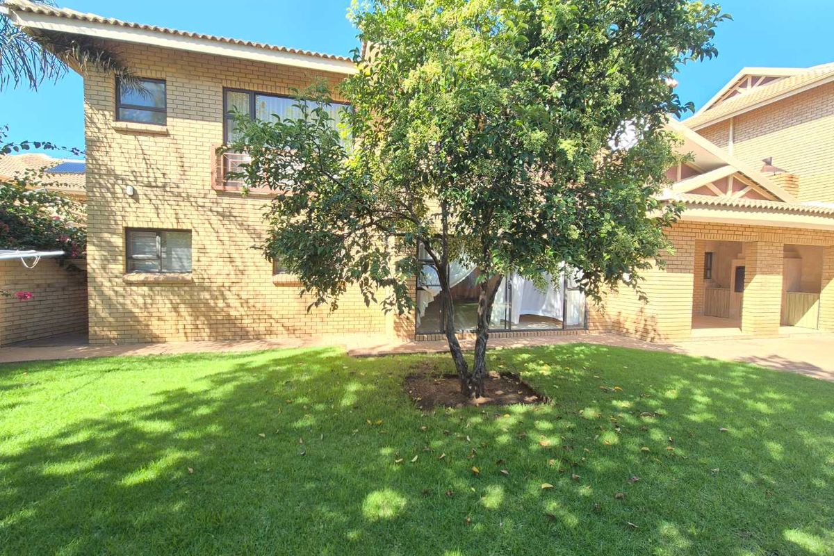 Rear view of the townhouse featuring face-brick exterior walls, sliding glass doors, and a private garden area with established tree.